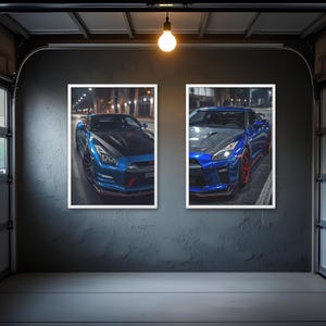 Puede incluir: Dos impresiones enmarcadas de coches deportivos azules se exhiben en una pared gris en un entorno de garaje. Los coches están estacionados en una calle de la ciudad por la noche, con faros y farolas que iluminan la escena. Los coches tienen capós negros y detalles en rojo.