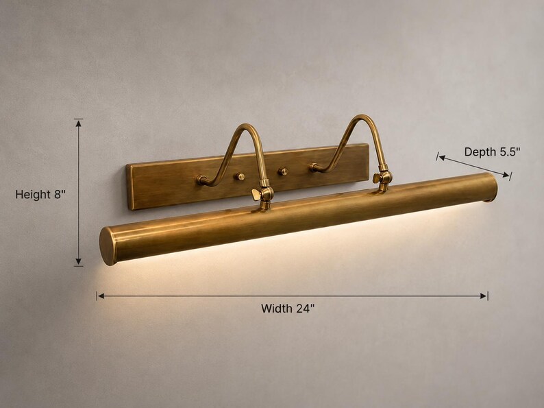 May include: A brass picture light with a rectangular wall mount, two curved support arms, and a cylindrical lamp head. The fixture measures 24 inches in width, 8 inches in height, and 5.5 inches in depth, featuring an integrated light source.