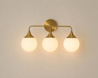 Puede incluir: Un aplique de pared de tres luces con una placa circular de latón y un brazo horizontal de latón. Tres globos de cristal esféricos de color blanco cuelgan del brazo, cada uno rematado con una tapa de latón festoneada que se une al aplique.