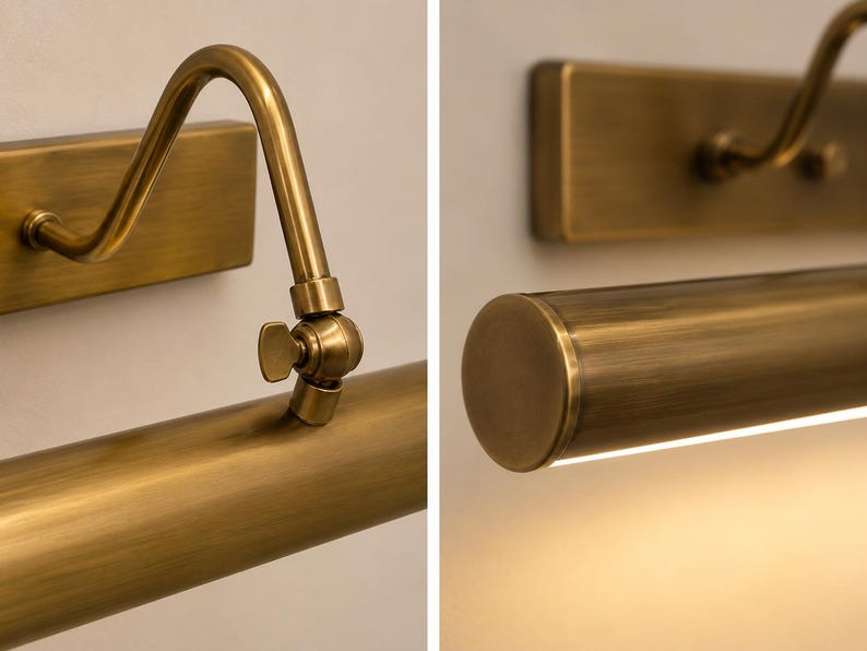 May include: A wall-mounted picture light with a brushed brass finish. The fixture features a rectangular backplate, a curved arm, and a cylindrical light housing with an adjustable wing nut hinge for positioning the angle of the light.