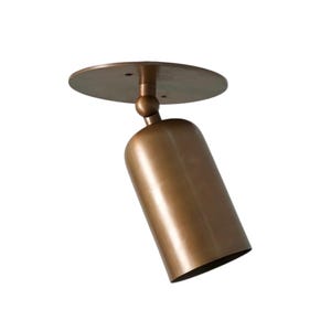 Puede incluir: Un foco de techo de color bronce con una pantalla cilíndrica y una placa de montaje circular. El foco está inclinado hacia abajo y el acabado tiene un brillo metálico. El diseño es moderno y minimalista.