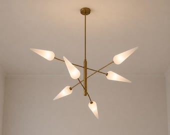 May include: A brass chandelier featuring a central vertical rod with six radiating arms, each ending in a conical, frosted white glass shade. The fixture is suspended from a matching brass canopy and emits a soft, diffused light from each point.
