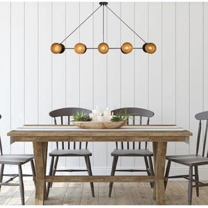 May include: A dining room scene featuring a wooden table and four gray chairs. Above the table hangs a black chandelier with five globe lights. A centerpiece of candles and greenery sits on the table.