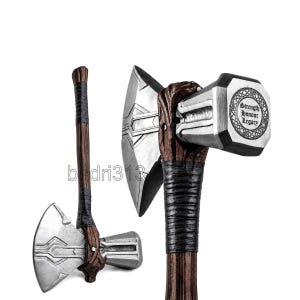 May include: A double-headed battle axe with a silver-colored metal head and a brown, wood-textured handle wrapped in black cord. The side of the axe head features a circular emblem with the engraved text Strength Honour Legacy.