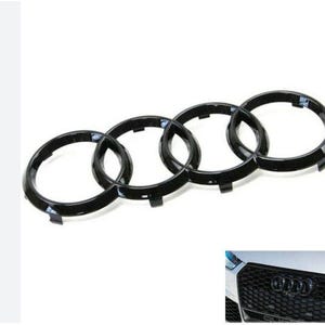 May include: Black car emblem featuring four interlocking rings. The emblem is a glossy black and is designed to be mounted on a vehicle's grille. The image also includes a close-up of the emblem on a car's grille.