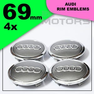 Può includere: Quattro emblemi per cerchi Audi argentati. Ogni emblema è circolare con il logo Audi al centro. Gli emblemi hanno un diametro di 6,9 cm. Il testo "AUDI RIM EMBLEMS" è visualizzato in alto a destra.