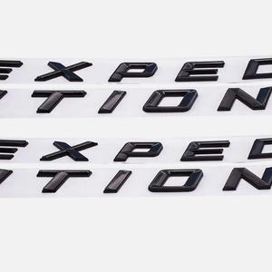 Op de afbeelding: Zwarte Expedition-embleemletters op zelfklevende strips. De letters zijn in een vetgedrukte blokstijl, ontworpen voor automobieltoepassingen. De afbeelding toont meerdere sets van de letters, klaar voor installatie.
