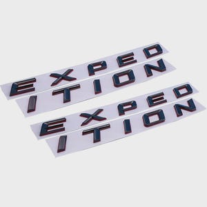 Op de afbeelding: Vier sets zwarte en rode "EXPEDITION" letters, elk op een witte achtergrond. De letters zijn glanzend en driedimensionaal, met een rode omtrek. De achtergrond is effen lichtgrijs.