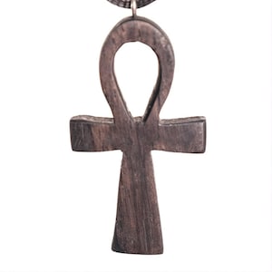 Peut inclure: Pendentif ankh en bois brun foncé, symbole de vie, suspendu à un cordon noir. L'ankh est sculpté avec un grain de bois visible et comporte une boucle en haut, une barre horizontale et une base verticale.