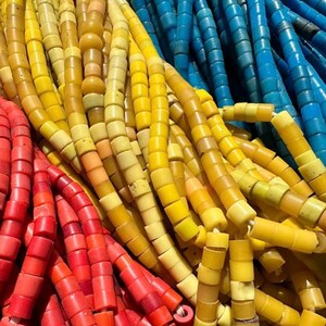 May include: Close-up of colorful beaded strands in shades of red, yellow, and blue. The beads are cylindrical and strung together, creating a textured and vibrant display. The beads appear to be made of glass or a similar material.