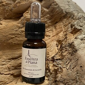 Può includere: Una piccola bottiglia di vetro marrone di olio essenziale di lavanda con tappo nero e contagocce trasparente. L'etichetta recita "Essenza di Piana" e "Olio Essenziale di Lavanda". La bottiglia contiene 10 ml di olio.