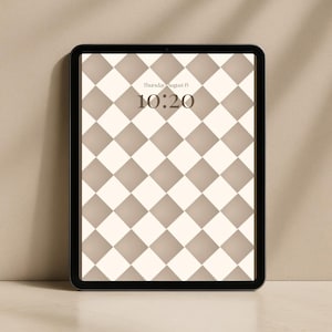 Op de afbeelding: Een zwarte tablet toont een digitale achtergrond met een herhalend ruitpatroon in beige en gebroken wit. De tijd is 10:20 uur en de datum is donderdag 15 augustus, weergegeven in een schreefletter. De tablet staat tegen een neutrale achtergrond.