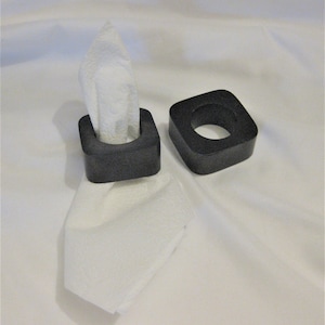 May include: Two black square napkin rings. One ring is holding a white napkin.