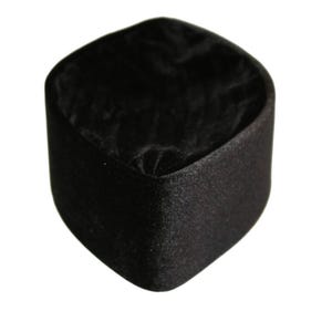 Op de afbeelding: Een klein, vierkant zwart sieradendoosje met afgeronde hoeken. De buitenkant heeft een matte, getextureerde afwerking, terwijl de binnenkant is bekleed met een zachte, donkerzwarte stof die bij de basis licht geplooid of gerimpeld oogt.