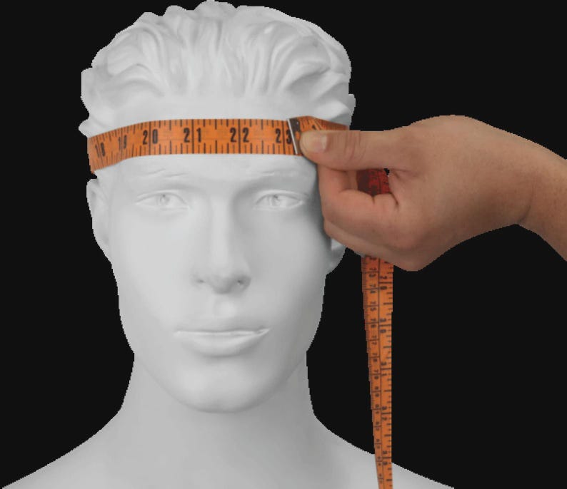 Op de afbeelding: Een wit etalagepophoofd met een gestructureerd kapsel. Een oranje meetlint is om het voorhoofd gewikkeld en toont een afmeting van ongeveer 58,4 cm. Het lint is voorzien van zwarte cijfers en lijnen voor een nauwkeurige hoofdomtrek.