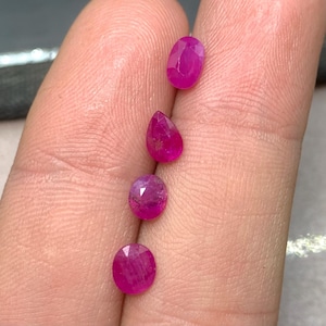 Op de afbeelding: Vier gefacetteerde robijnen in ovale en peervormige vormen. De edelstenen hebben een levendige, dieproze-rode kleur. De edelstenen worden tegen een neutrale achtergrond gepresenteerd.