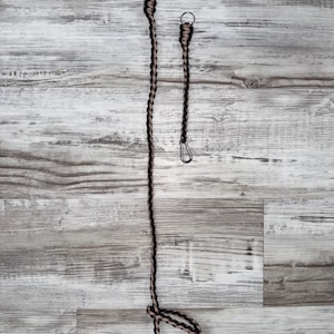 May include: Two braided paracord lanyards. One is long with a loop at the bottom and a metal clip and ring at the top. The other is shorter with a metal clip and ring. The paracord is black and tan.