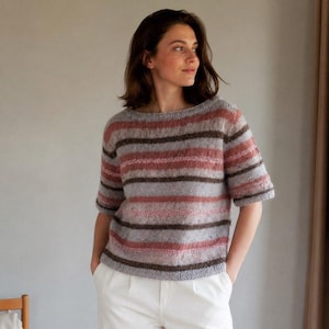 Pode incluir: Uma camisola de malha de manga curta com riscas horizontais em tons de rosa seco, cinzento claro e castanho escuro. A peça tem um decote redondo, uma bainha canelada e um aspeto felpudo e suave com um corte descontraído.