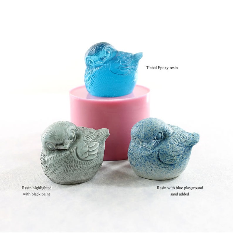May include: Three bird figurines made with resin. The first bird is a light blue color and is made with tinted epoxy resin. The second bird is a light gray color and is highlighted with black paint. The third bird is a light blue color with blue playground sand added.