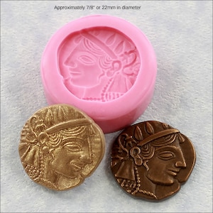 May include: A pink silicone mold for making a round coin with a detailed profile of a woman's face. The mold is 7/8 inch or 22 mm in diameter. Two examples of the coin are shown, one in gold and one in bronze.