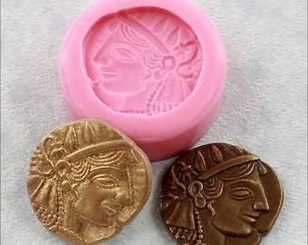 May include: A pink silicone mold for making a round coin with a detailed profile of a woman's face. The mold is 7/8 inch or 22 mm in diameter. Two examples of the coin are shown, one in gold and one in bronze.