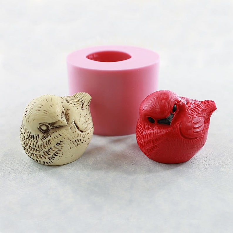 May include: Two small bird figurines, one red and one beige, with a pink silicone mold for making similar figurines.