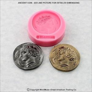 May include: Two silver and gold coins with a profile of a woman's face on each side. The coins are on a white surface. The coins are in a mold for making replicas.