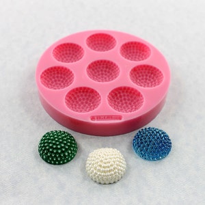 May include: Pink silicone mold with seven round depressions, each with a textured surface. Three round, textured, decorative balls in green, blue, and white.