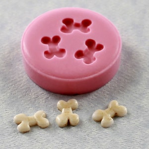 May include: Pink silicone mold with four bone-shaped cavities. Three white bone-shaped candies are shown next to the mold.