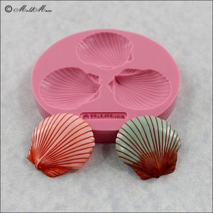 May include: A pink silicone mold with three scallop shell shapes. Two finished scallop shell shapes are shown, one with red and white stripes and the other with green and brown stripes.
