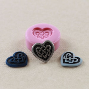 May include: A silicone mold for making heart-shaped resin crafts. The mold is pink and has a Celtic knot design. There are three finished resin hearts, one silver, one blue, and one light blue.