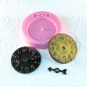 May include: Two gold-colored clock face charms with black Roman numeral markings and a black arrow hand. A pink silicone mold with a clock face design and a gold-colored arrow charm.