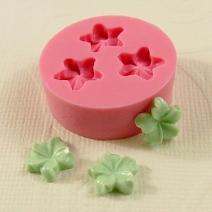 May include: A pink silicone mold with three star-shaped cavities. Three green star-shaped candies are next to the mold.