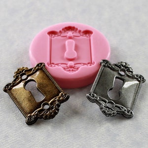 May include: Two decorative keyhole plaques, one gold and one silver, with ornate floral designs. A pink silicone mold with the same design is also shown.