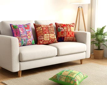 May include: Four square throw pillows featuring intricate patchwork designs with embroidered details. One pillow is purple and multicolored, two are shades of red and gold, and one is green and gold, all displaying varied floral and geometric patterns.