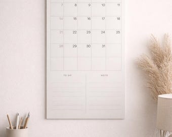 May include: A white wall calendar for February 2026, hanging on a wall. The calendar has a simple design with the month and year at the top, and the days of the month in a grid. A mug, pencils, and books are on a wooden desk.