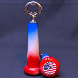 May include: A bottle opener with a chrome top and a red, white, and blue handle. Next to it is a red, white, and blue round object with the text "Treats" and an American flag design.