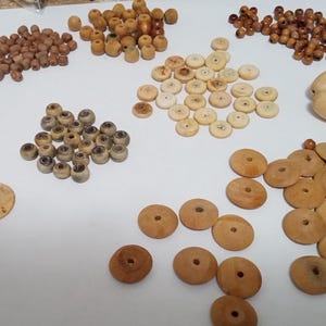 May include: A collection of various wooden beads and buttons in shades of brown and beige. The assortment includes round beads, disc-shaped buttons with holes, and oval-shaped beads, ideal for crafting and jewelry making.