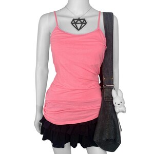 May include: A mannequin displays a pink spaghetti strap tank top, a black ruffled mini skirt, and a dark denim shoulder bag. A black diamond pendant necklace and a white plush bunny bag charm complete the outfit.
