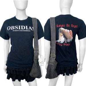 May include: Black t-shirt with the word "OBSIDIAN" and a website address printed in white. The shirt is paired with a black denim shoulder bag and a black ruffled skirt. The back of the shirt has a graphic with the text "Longer An Angel".