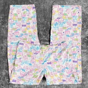 Puede incluir: Pantalones de pijama blancos con un colorido estampado de cupcakes. Los cupcakes son en tonos rosa, azul, amarillo y morado. Los pantalones tienen un corte holgado y están hechos de un material suave.