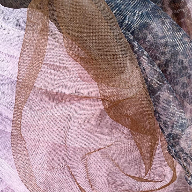 May include: Close-up of layered sheer fabrics in shades of pink, brown, and gray. The fabrics have a delicate, airy texture, with a subtle sheen. The arrangement creates a sense of depth and visual interest, suitable for fashion or craft projects.
