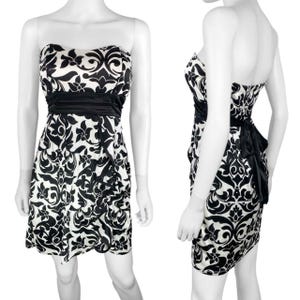 Puede incluir: Un vestido sin tirantes con estampado en blanco y negro. El vestido presenta una cinturilla de satén negro y un lazo negro en la espalda. El estampado es un diseño floral. El vestido se exhibe en un maniquí.