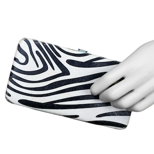May include: A white and black zebra print wallet. The wallet is rectangular and has a clasp closure. The zebra print pattern is bold and graphic, with black stripes on a white background.