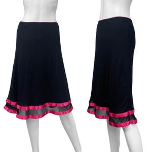 May include: A black skirt with a pink trim at the waist and hem. The hem features a sheer gray panel with a pink satin ribbon border. The skirt is displayed on a mannequin.