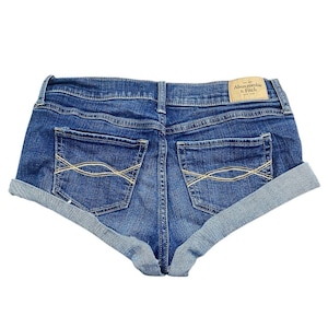 May include: Blue denim shorts with rolled cuffs. The shorts have two back pockets with a decorative stitch design and a small label on the back. The shorts are made of a medium-wash denim material.