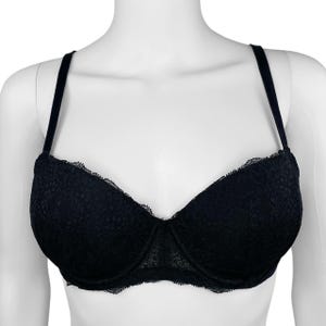May include: Black lace bra with adjustable straps. The bra features a delicate floral lace pattern and a scalloped edge along the cups. The straps are thin and black, and the bra is displayed on a white mannequin.