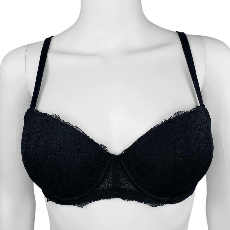 May include: Black lace bra with adjustable straps. The bra features a delicate floral lace pattern and a scalloped edge along the cups. The straps are thin and black, and the bra is displayed on a white mannequin.