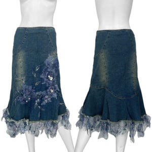 May include: Two denim skirts with a flared hem and floral embellishments. The skirts are a medium wash blue with a distressed look. One skirt features a large floral design with blue sequins and beads. The hem is trimmed with a sheer, ruffled fabric.