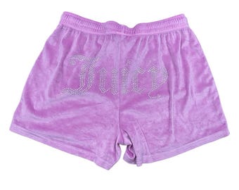 May include: Lilac velour shorts with an elastic waistband. The word "Juicy" is spelled out in silver rhinestones across the back of the shorts. The shorts are a soft, casual style.